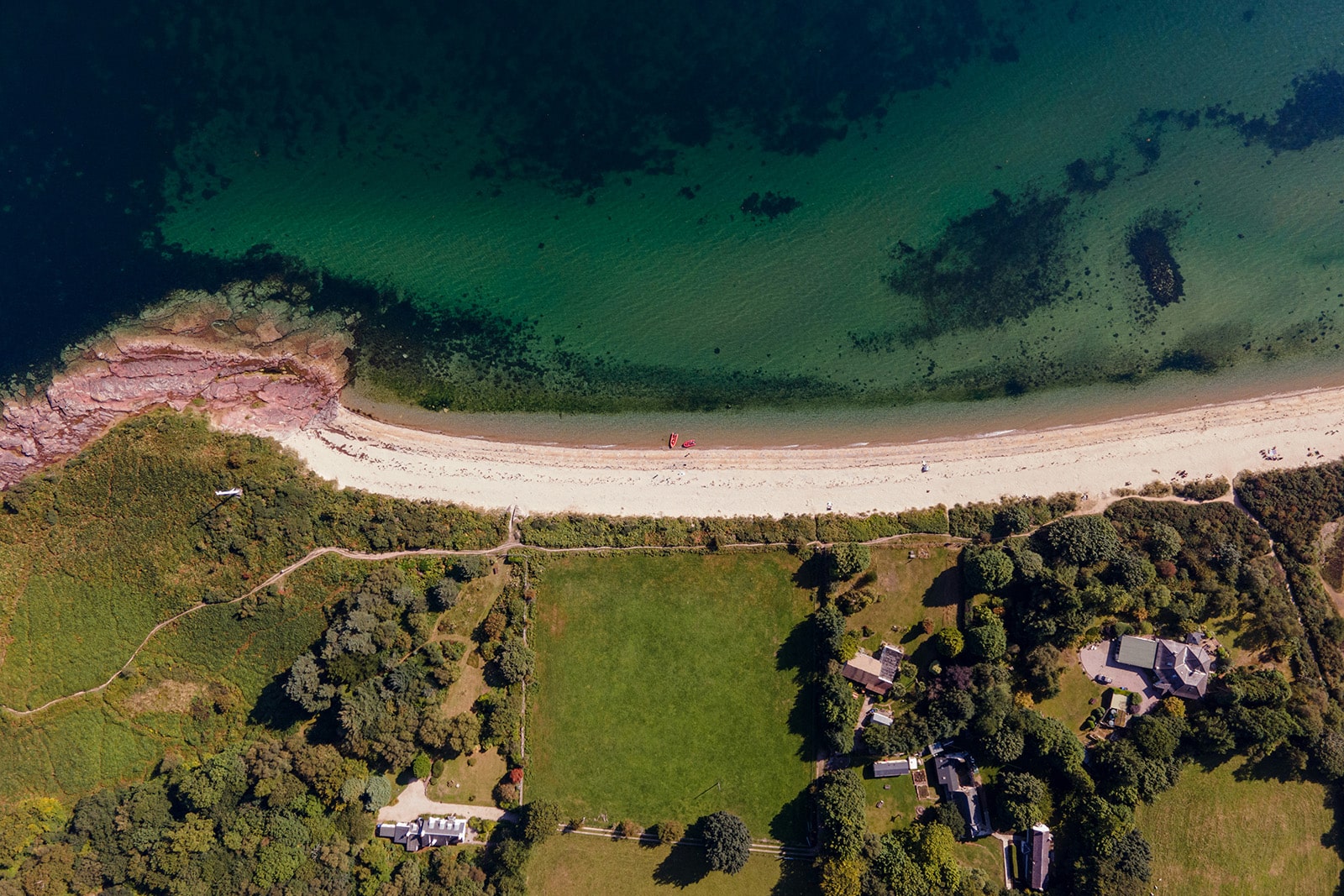 An aerial view of Sannox Bay, Isle of Arran, dipicting half a dozen steadings, a white sand beach, and a deep turquiose sea