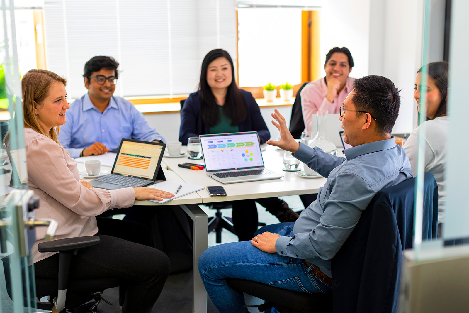 A group of individuals seated at a table, with pens and paper to hand and laptops preloaded with presentations