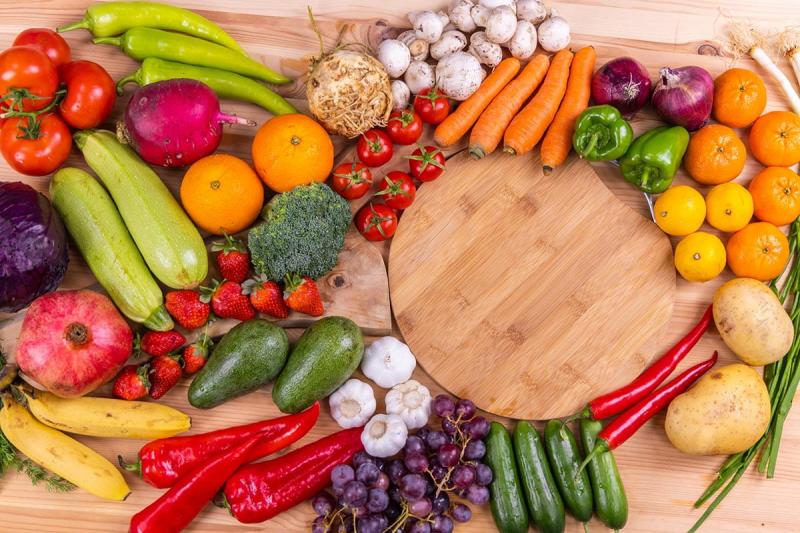 A chopping board surrounded by different fruit and vegetables.